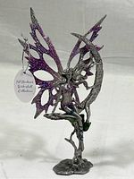 Metal fairy figure sculpture with purple glittered wings, seated on crescent moon with ivy details.