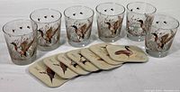 Photo shows six clear glass cocktail glasses with mallard duck in flight design, flying birds near the rim, and seven plastic coasters with various waterfowl images in front of glasses.