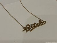 Close-up showing the gold pendant with the word 'Bitch' and a small diamond dotting the 'i'.