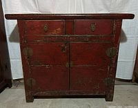 Front view of red lacquer dresser with two top drawers and double-door cabinet below, showing brass hardware and patina.
