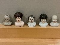 Five antique miniature doll heads lined up, showing size and detail of each with varying hair styles and paint wear.