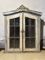 Front view of antique shabby chic French medicine cabinet showing double glass paneled doors and decorative crest.