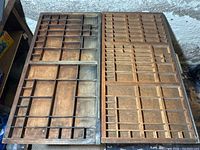 Pair of antique wooden printing trays side by side, showing segmented compartments of various sizes for typesetting or organizing small items.