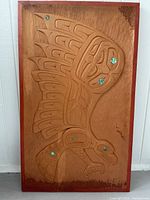Full front view of carved wood plank with red-painted border and abalone inlays