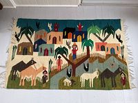 Full view of handwoven colorful rug with village houses, palm trees, animals, and people