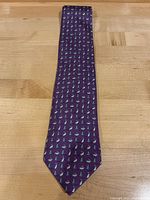 Full view of purple Hermes silk tie laid flat demonstrating overall pattern and shape.