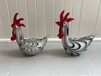Front view of two Murano glass rooster figures showing detailed red combs and black swirl patterns on white glass bodies.