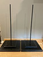 Pair of black wood square bases with black metal rods as mask displays on a wooden surface.