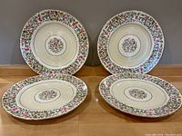 Four Royal Crown Derby Cotswold floral dinner plates arranged on a wooden floor showing the complete set and floral design pattern.