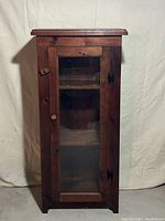 Front view of the antique wooden cabinet with glass front and three interior shelves showing lock and knob details.