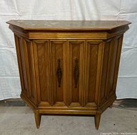 Full front view of vintage 1960s small wooden cabinet with two doors, paneled sides, and inset marble top taken against white backdrop.
