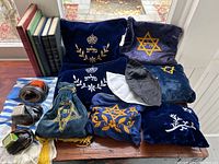 Overview of vintage Judaica lot showing books, tallits, velvet tefillin bags with embroidery, leather straps, and kippot bag.