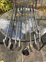 Photo of all golf clubs laid out on a glass patio table, showing full length shafts and club heads.