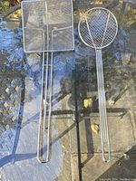 Photo of rectangular and round stainless steel mesh fry strainers with long handles on glass table.