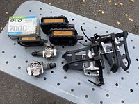 Photo of Shimano clip-on pedals with reflective panels, flexible toe baskets, and a boxed Presta inner tube on perforated metal surface.