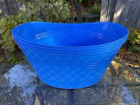 Single large blue plastic tub showing textured exterior and hand grips, placed outdoors on a stone surface.