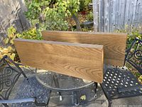 Two custom made oak veneer floating shelves displayed outdoors on a black metal table, showcasing the front face and natural oak wood grain.