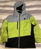 Front view of Descente youth ski jacket showing color blocking in grey, yellow-green, and black with zippered front and hood.