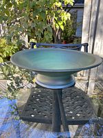 Side view of the handmade ceramic display dish placed outdoors, showing its pedestal base and green glaze.