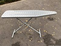 Metal ironing board with perforated top surface and cross legs on asphalt background