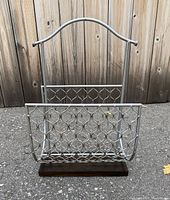 Front view of the metal and wood magazine holder showing woven metal basket and wooden base with handle