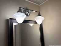 Dual-light polished nickel wall fixture attached above mirror, showing sculpted white glass globes