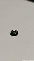 Photo showing oval cut sapphire on white surface under natural lighting highlighting green with blue undertone.
