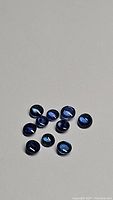 Photo of 11 round cabochon cut blue sapphire gemstones with deep blue color, arranged scattered on white background.