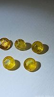 Photo showing five round cut natural canary yellow sapphires with bright yellow color and various minor inclusions, placed on white background under light.