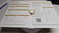 Photo of the moissanite ring on top of its GRA certification showing detailed grading info including 1 carat weight, D color, VVS1 clarity.