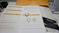 Ring positioned on open GRA certification showing pear shape diagrams and grading sheet