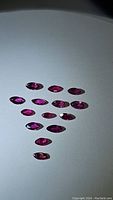 Photo showing 13 untreated rubies laid out on flat white background, highlighting vivid fuchsia tones and high clarity.