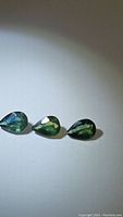 Three pear cut green to blue sapphires laid out on a white surface showing their color and clarity.