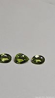 Three apple green peridot gemstones arranged on a plain surface, showing their color and faceting.