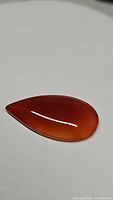 Single pear-shaped deep mandarin orange carnelian cabochon on white background