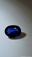 Close-up image of oval cut deep royal blue Ceylon sapphire on gray background showing facets and rich color.