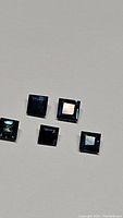 Five square cut blue sapphire gemstones arranged on a white background, showing facets and color.