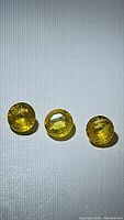Three natural yellow sapphire gemstones arranged side by side on a plain surface under direct light, showing facets and transparent yellow color.