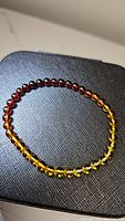 Front view of a stretch Baltic amber bracelet showing a gradient from yellow to dark reddish amber beads, approx 5mm each