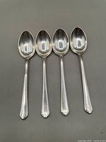 Four sterling silver teaspoons laid side by side showing overall shape and form.