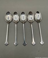 Top view of 5 sterling silver teaspoons laid side by side showing overall shape and design