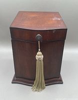 Closed top view of the upright dark wood jewelry box showing slightly curved front and tassel on the front lock.