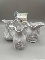 Lot of four ceramic creamers; three white bisque Portmeirion Parian Ware creamers with detailed raised relief and one yellowish cream Paragon china creamer with blue floral decoration.