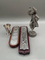 Four Judaica items on gray background: two mezuzahs, kiddush cup, Hasidic man figurine