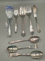 All eight pieces laid out on gray surface: two large serving forks, lunch fork in original bag, butter spreader and four teaspoons.