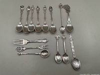 Overview of all 14 pieces including 12 spoons and 2 small forks displayed on gray background.