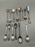 Overhead image of all 12 souvenir spoons showing variety in design, patterns, enamel, and markings.