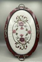 Full view of the oval serving tray showing the embroidered floral design under glass and wooden frame with metal handles.