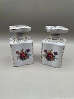 Front view of two square white porcelain dresser jars with floral designs and gold detailing.