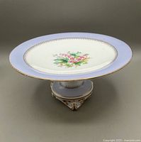 Porcelain tazza shown from above and side highlighting bleeding heart motif and violet gold-edged border with raised pedestal base.